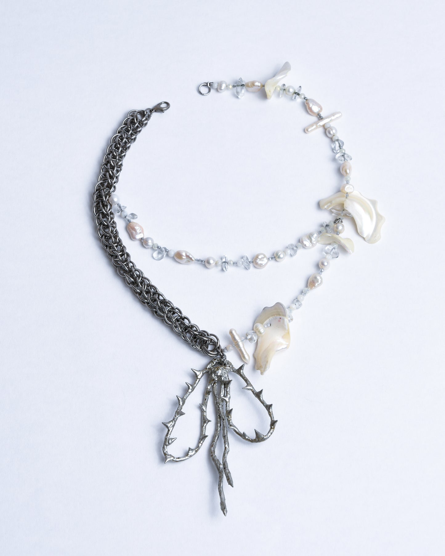 Necklace is split into silver stainless steel chainmail and 2 strings of a mix of white AAA+++ biwa fresh water pearls, salt water pearls, polished sea shells and crystals. Silver spiky bow pendant hanging on the bottom.