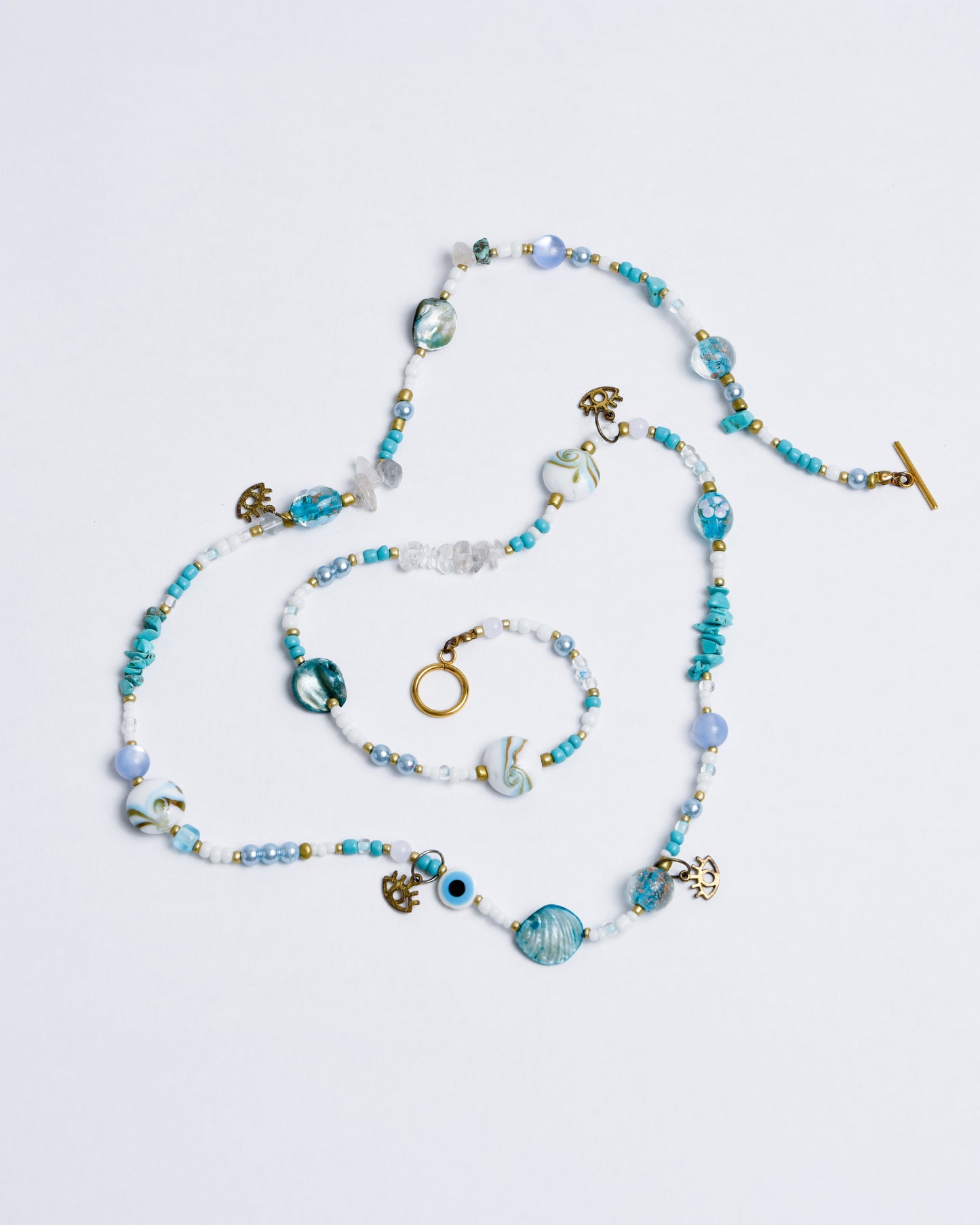 A blue, turquoise, and white beaded chain with gold accents and eye pendants, held together by a nylon cord and copper rings.