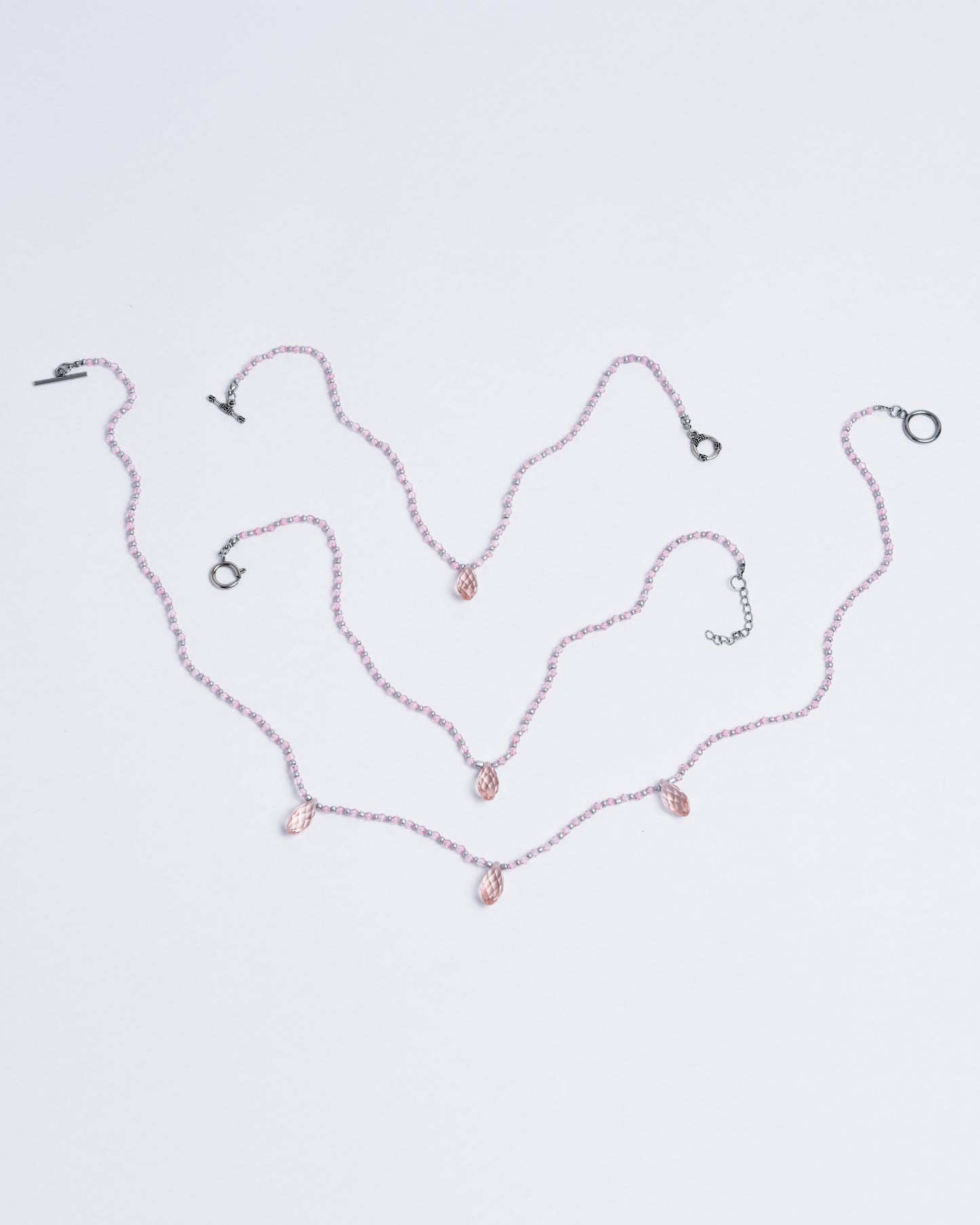 Pink glass drop beads serve as pendants, paired with pink plastic beads, silver glass beads, and silver copper closures on a nylon cord.