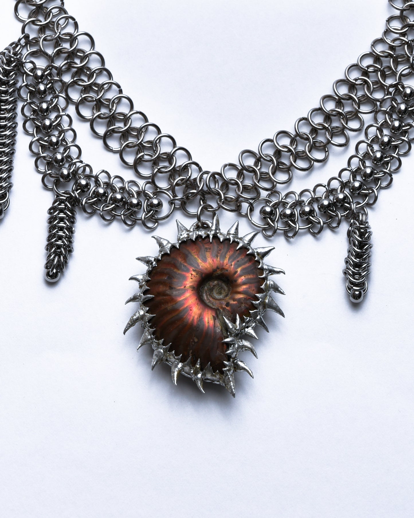 Closeup of red ammonite pendant adorned with silver spikes.