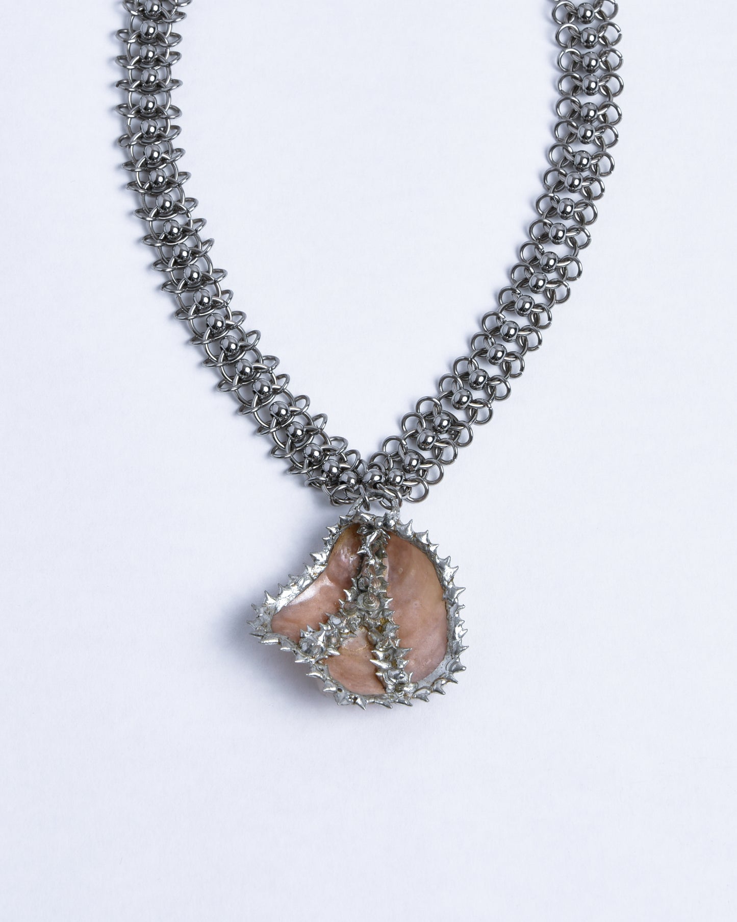 closeup of silver stainless steel chainmail necklace with spiky champagne pink mother of pearl sea shell pendant