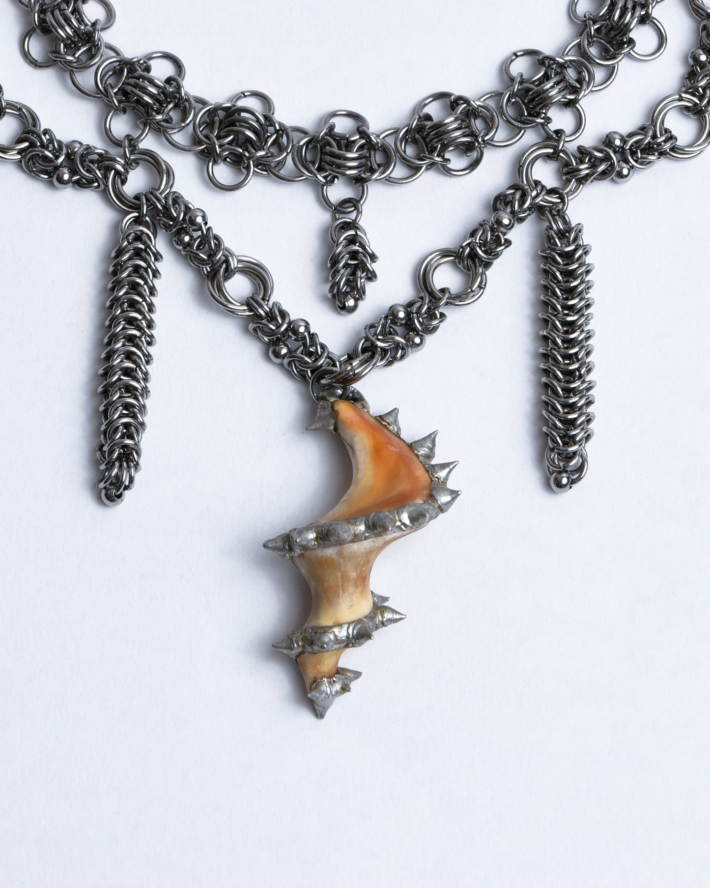 Closeup of pendant is made from middle part of sea snail shell which is orange and cream colored adorned with spikes using silverlead-free Sn99Cu1 soft solder
