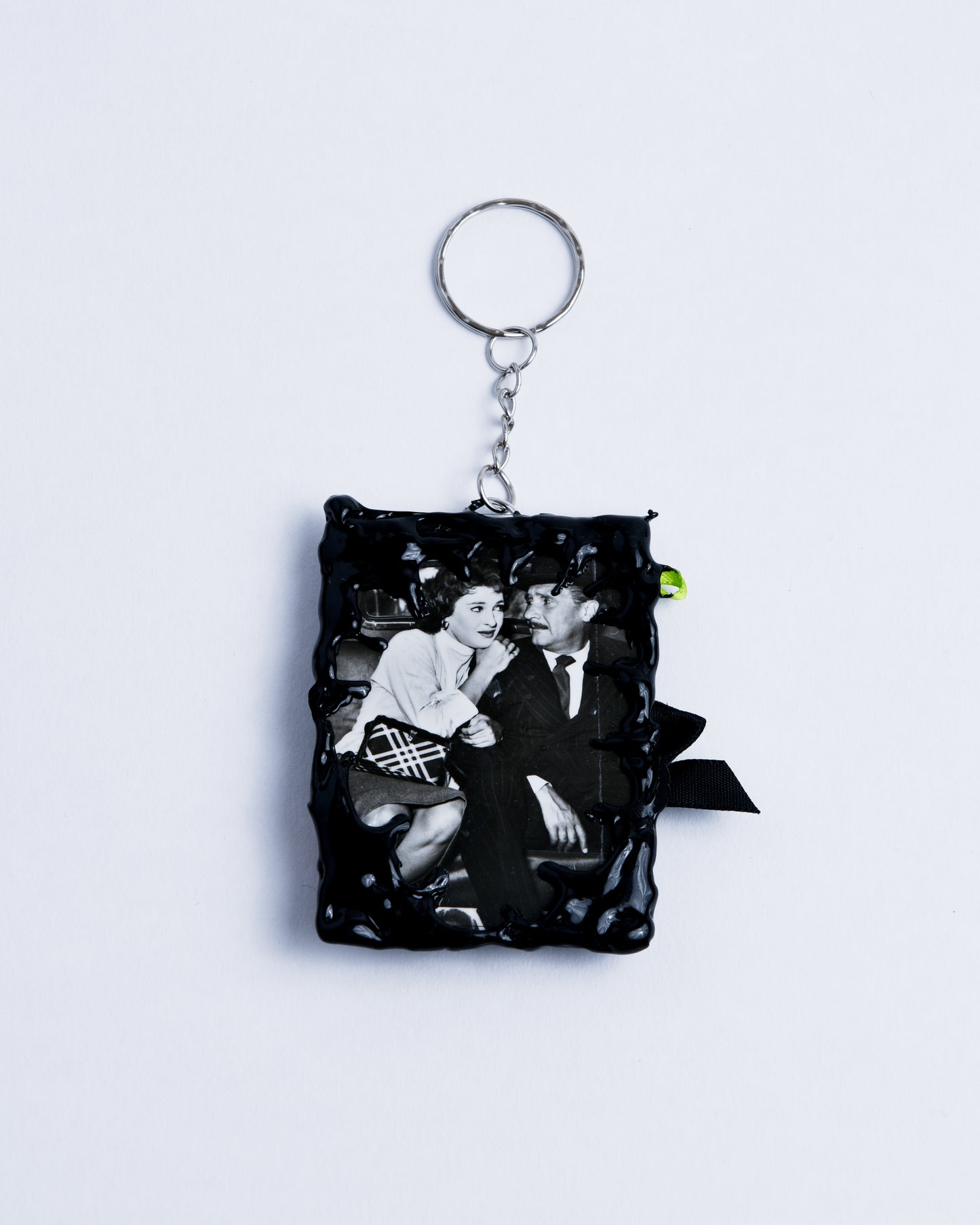 Black-and-white picture of a couple, framed in black hot glue rectangle frame. Stainless steel rings serve as the keychain part, holding the piece together.