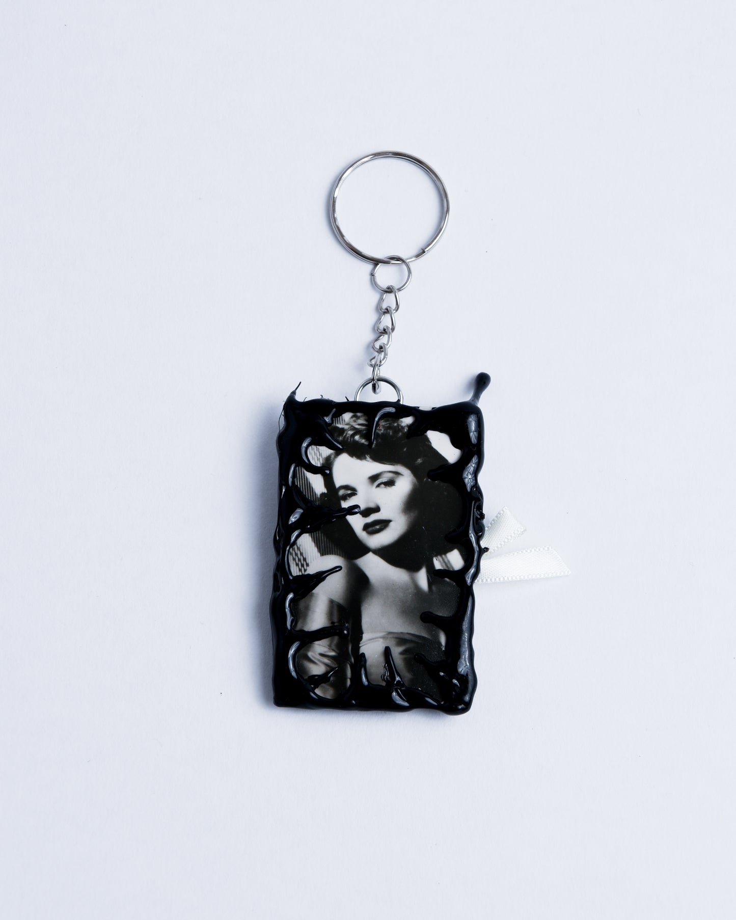 Black and white picture of a woman framed in black hot glue Stainless steel rings are the keychain part holding the piece together.