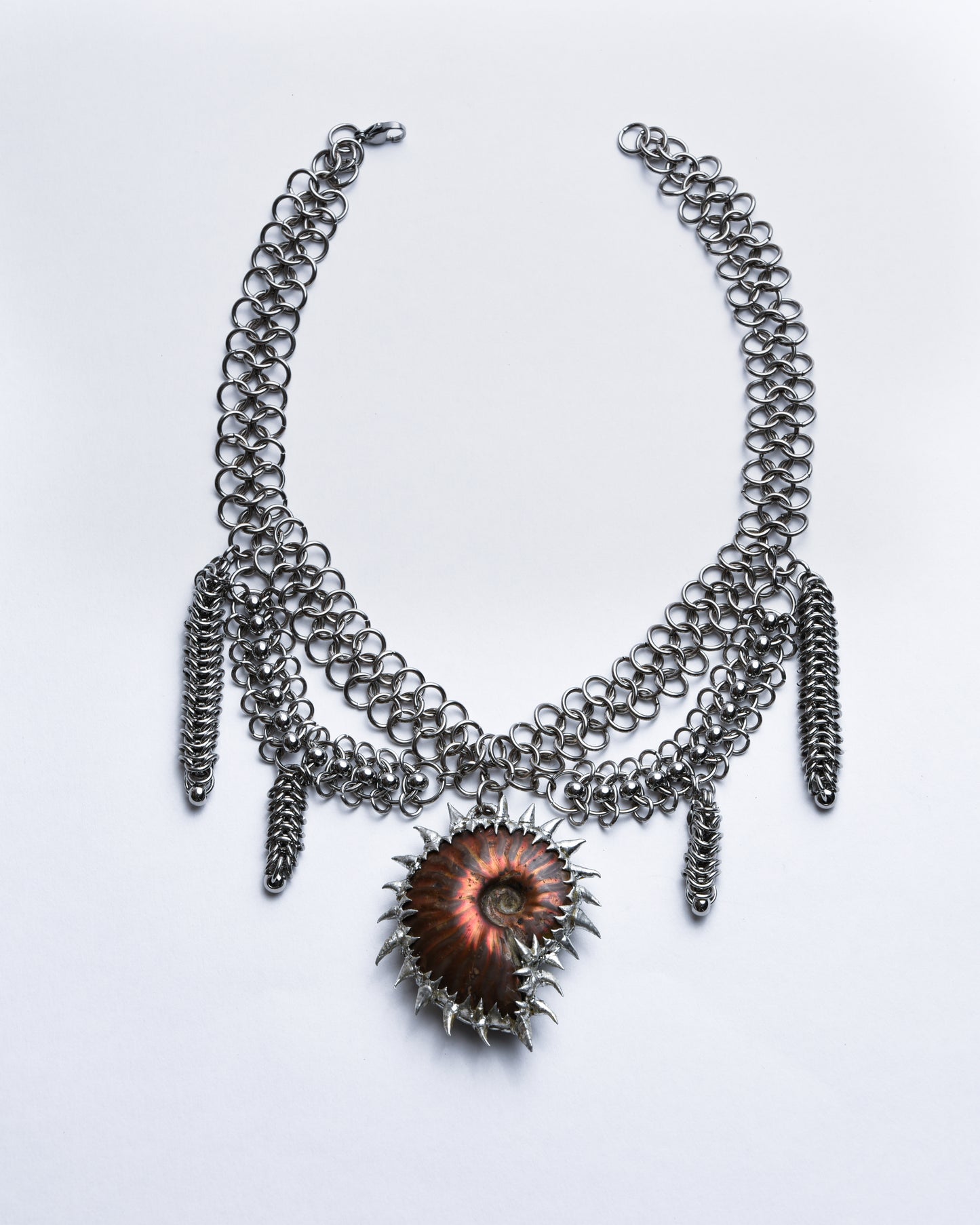 Silver chainmail necklace with red ammonite pendant adorned with silver spikes.