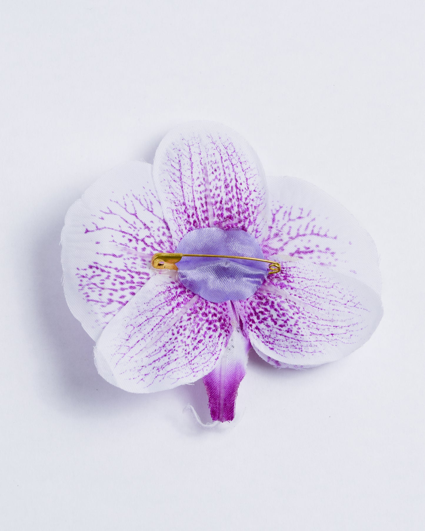 back of white and purple dotted fabric orchid flower attached to pin with soft fabric.