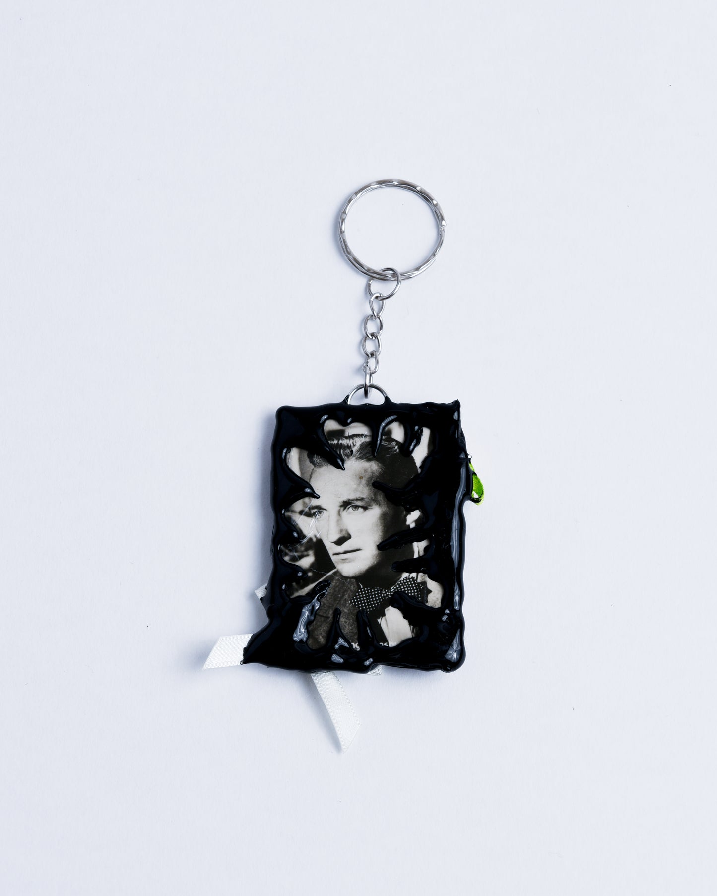 Black and white picture of a man framed in black hot glue. Stainless steel rings are the keychain part holding the piece together.