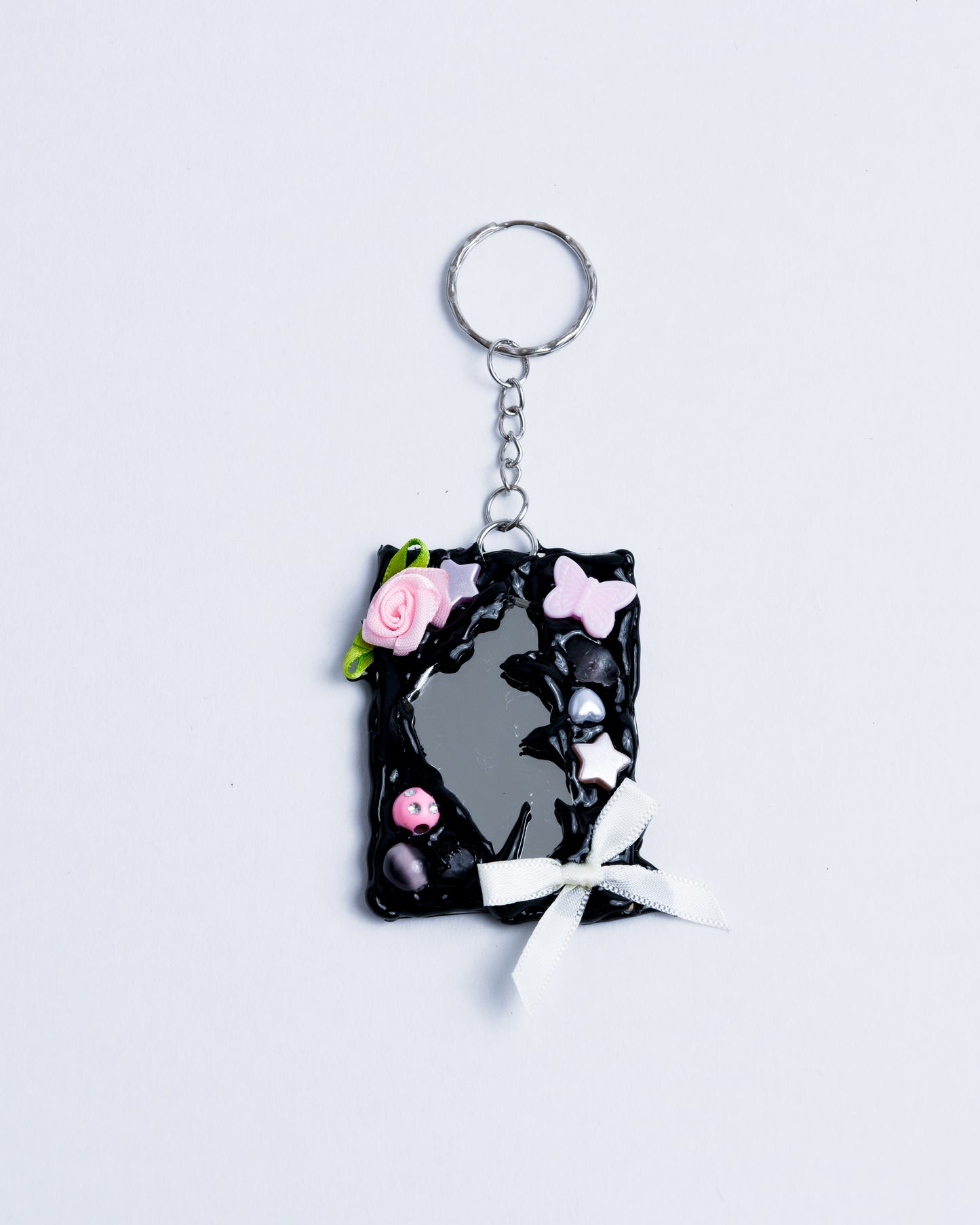 black hot glue frame with beads, pearls and little fabric bows to surround the broken mirror piece on the back. Stainless steel rings are the keychain part holding the piece together.