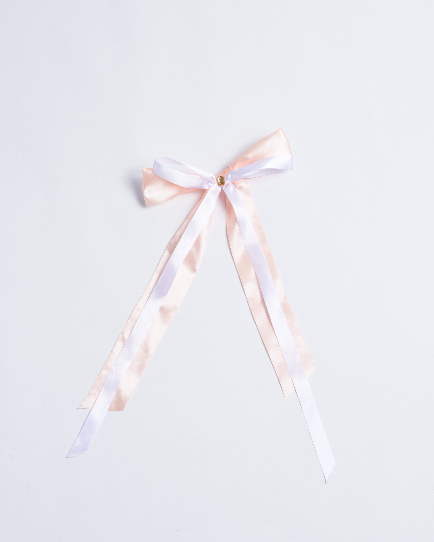 Salmon-colored fabric bow with a small plastic crystal, fixed onto gold metal pins.
