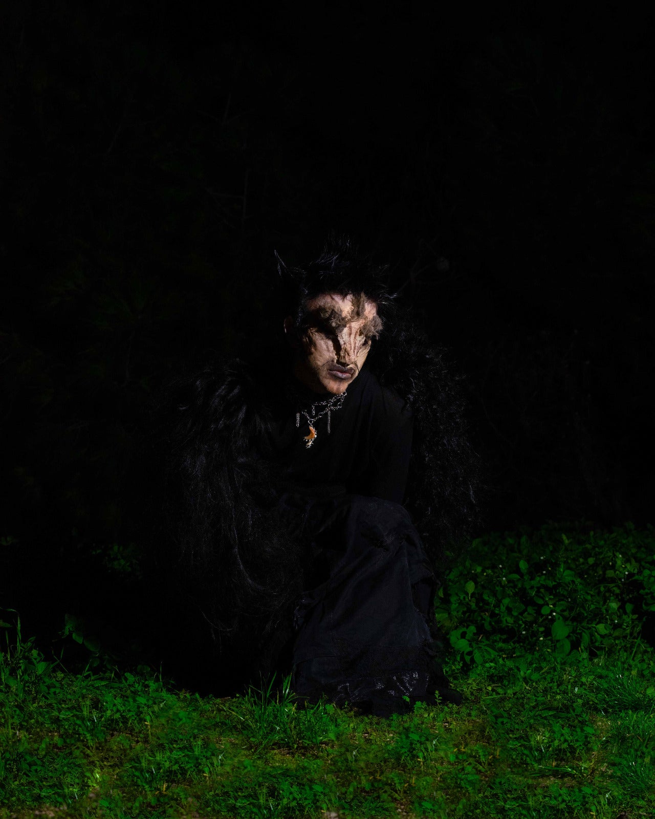 model wears spiral of the abyss necklace in a creature costum sitting on grass