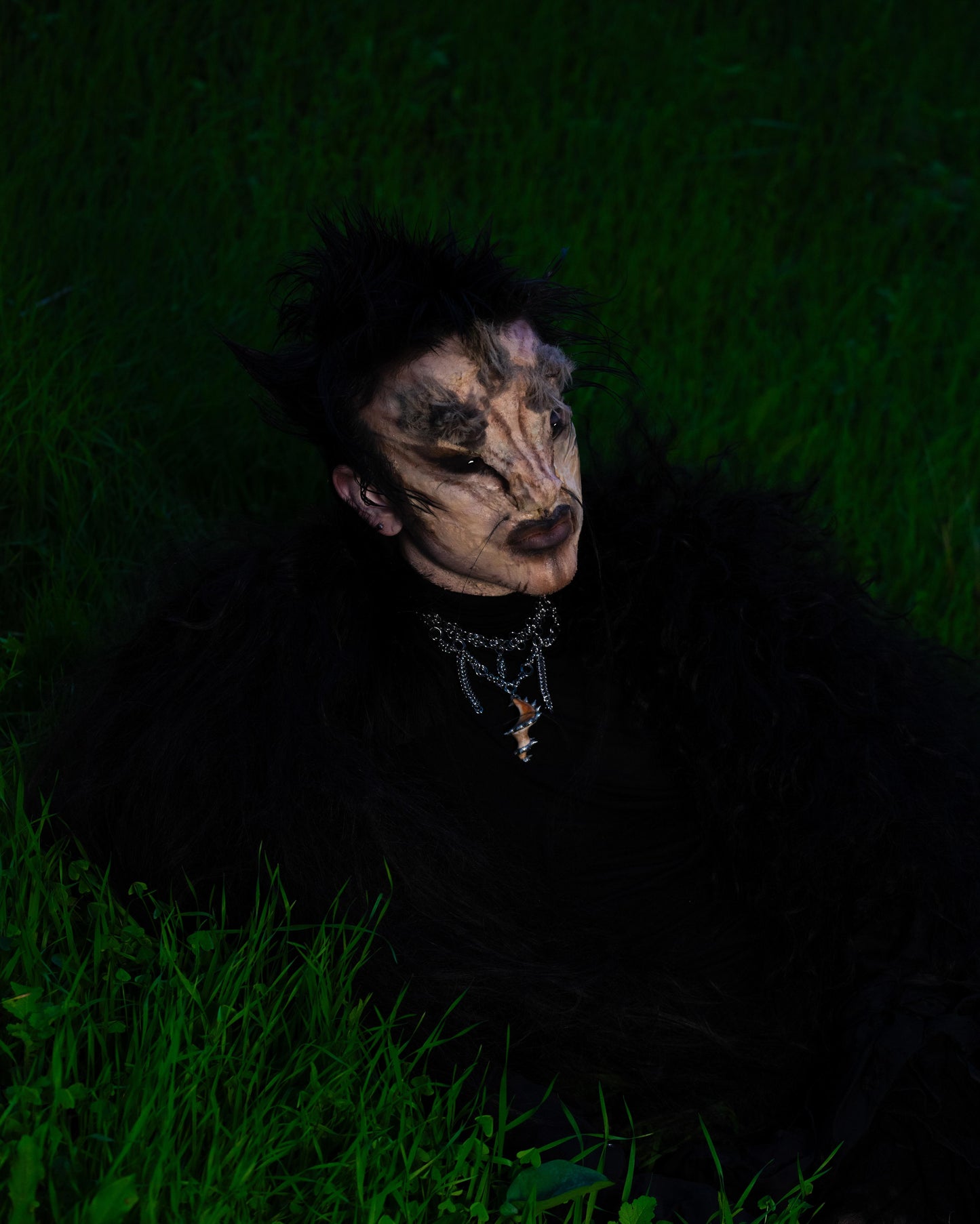 model wears spiral of the abyss necklace in a creature costum laying in grass
