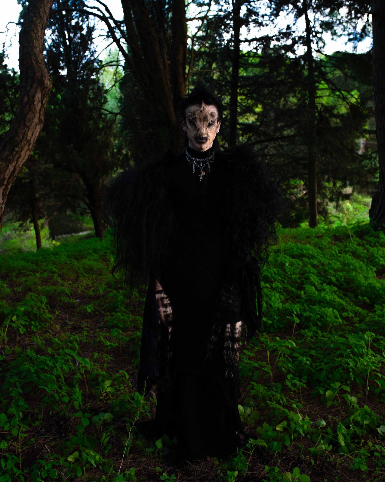 model wears spiral of the abyss necklace and harschuri bussi in a creature costum standing on grass