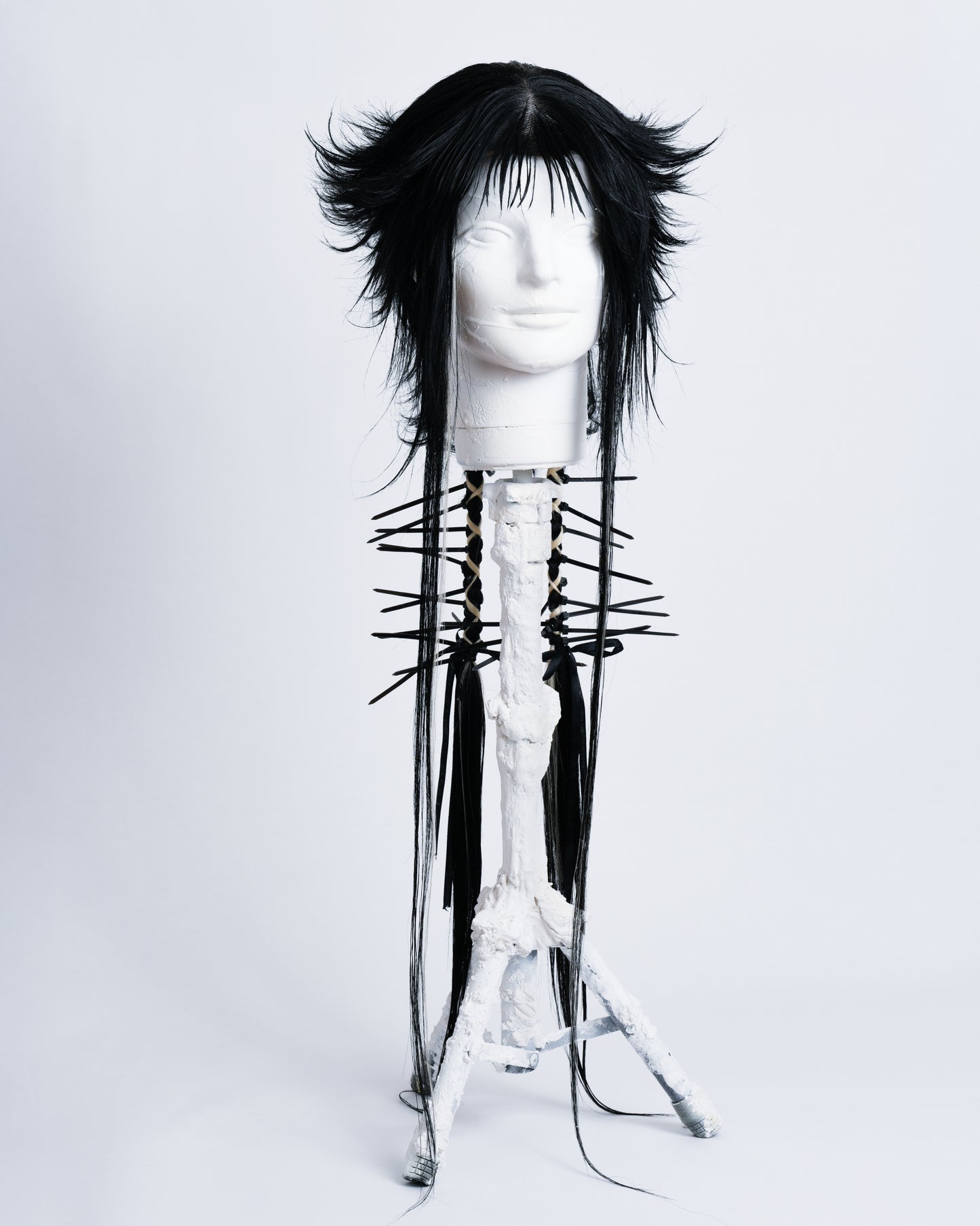 WIG Ren is a 70cm long anime cut black wig with bangs and two braids in the back with white highlights braided in and black cable ties coming out .