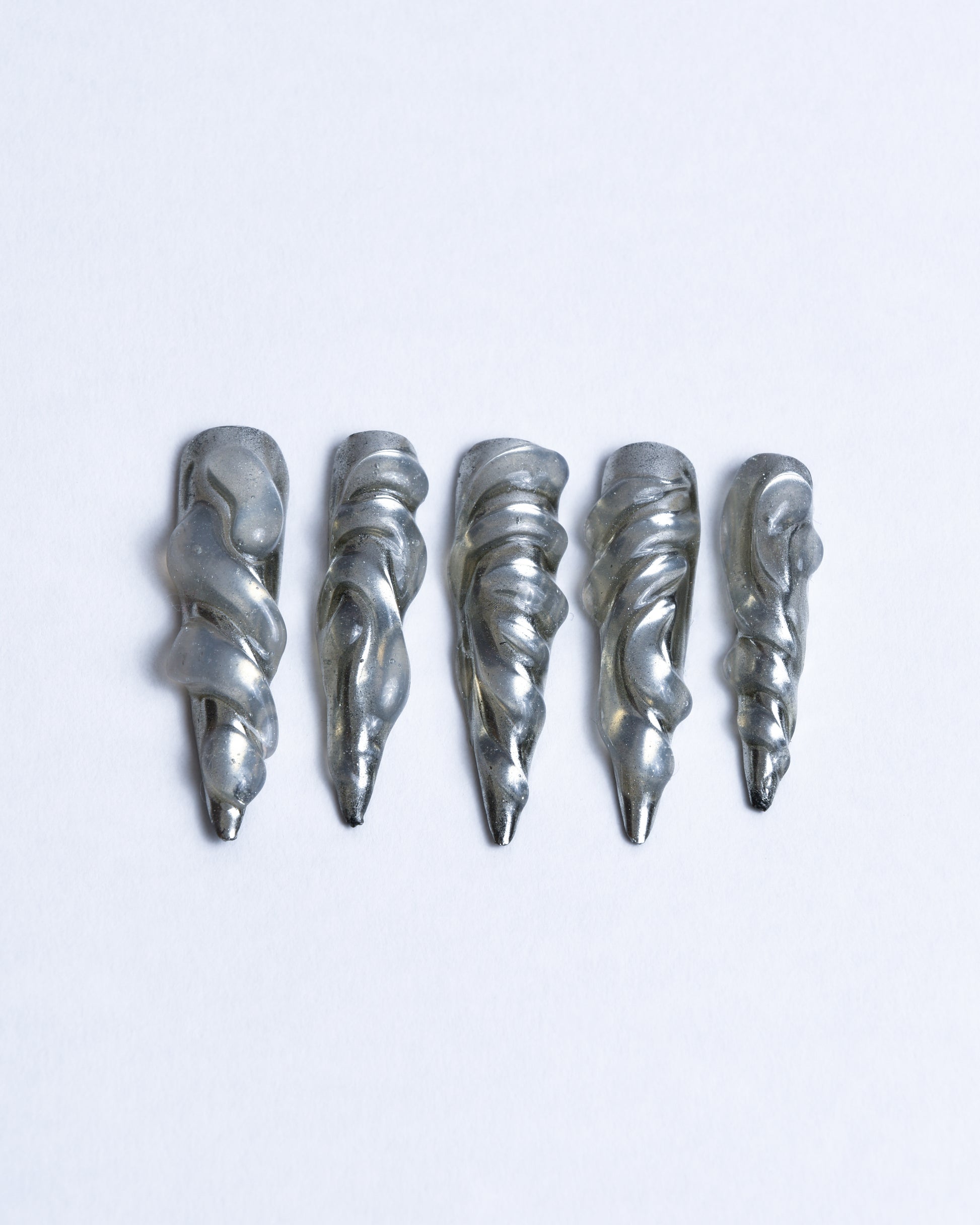 Long stiletto chrome silver nails with 3D transparent waves design for futuristic, alternative cyber look daily or editorial use crafted with a transparent wavy base and topped with a silver chrome finish. 